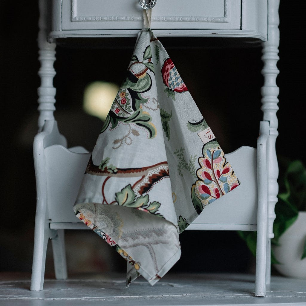 Linge à main de couleur fleurs colorées suspendu sur petit meuble en bois blanc.