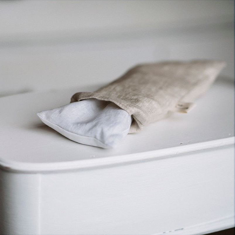 Petit coussin apaisant couleur naturelle avec pochette ouverte sur meuble blanc.