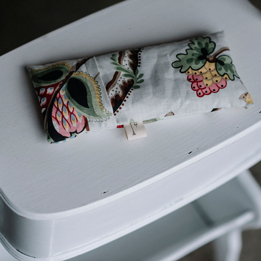 Petit coussin apaisant tissu fleurs colorées sur meuble blanc vu d'en haut.