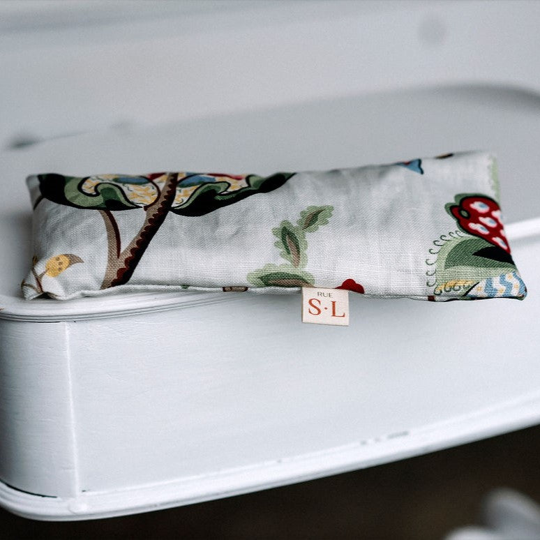 Petit coussin apaisant couleur fleurs colorées avec étiquette SL sur meuble blanc.