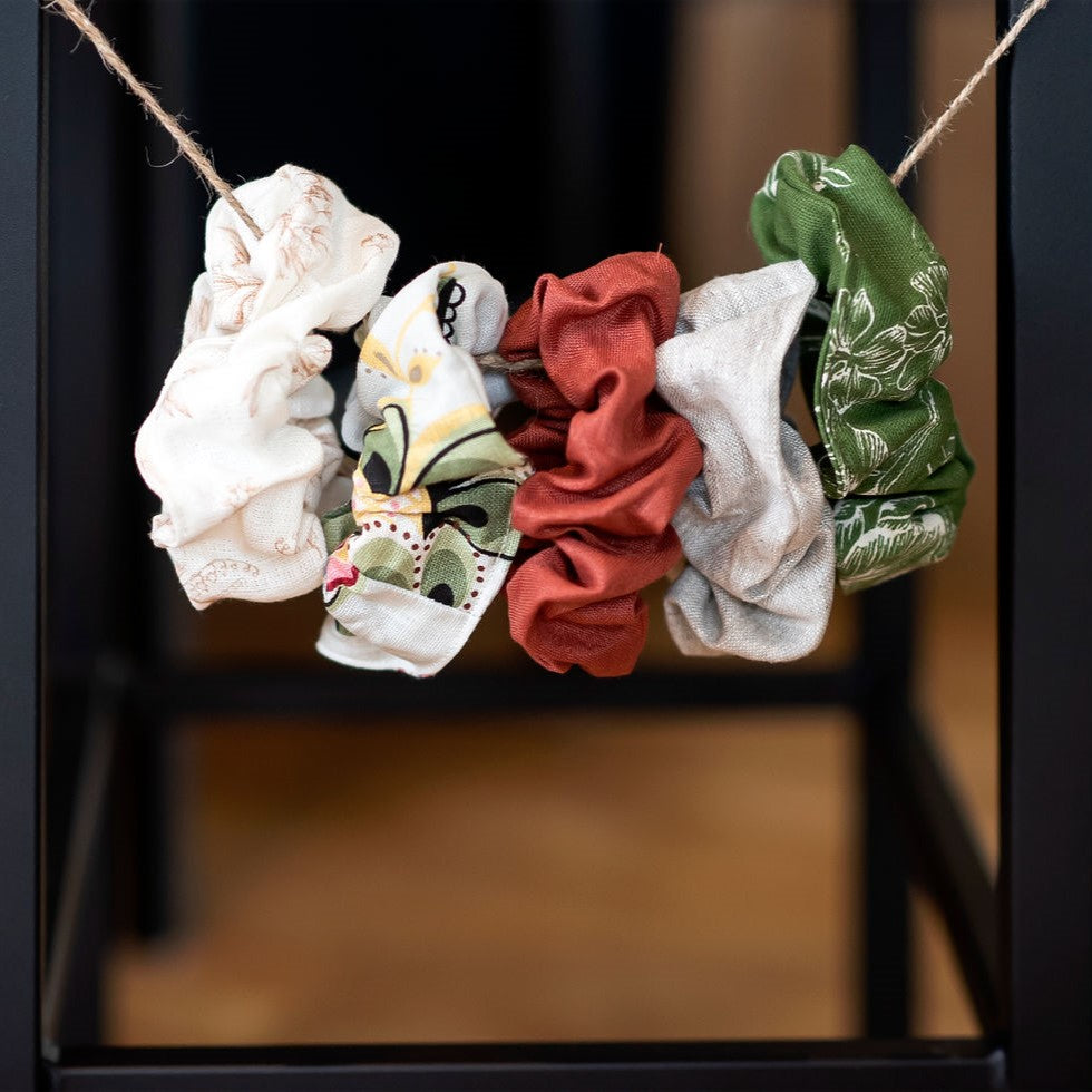 Série de chouchous à cheveux en lin de différentes couleurs suspendus sur corde.