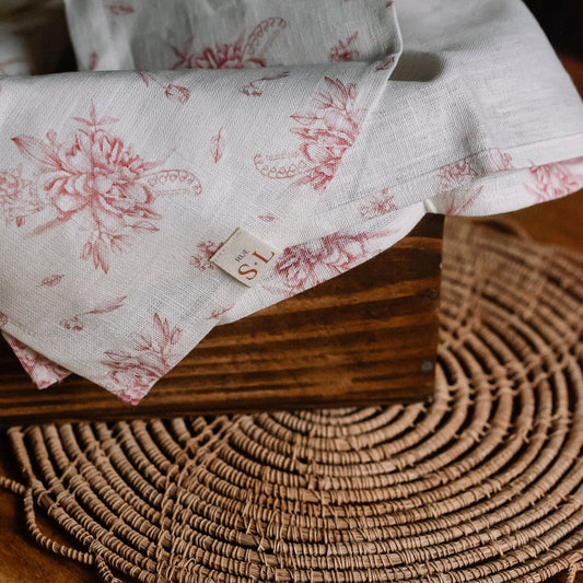 Linge à vaisselle avec fleurs framboises dans boîte en bois sur napperon rond.