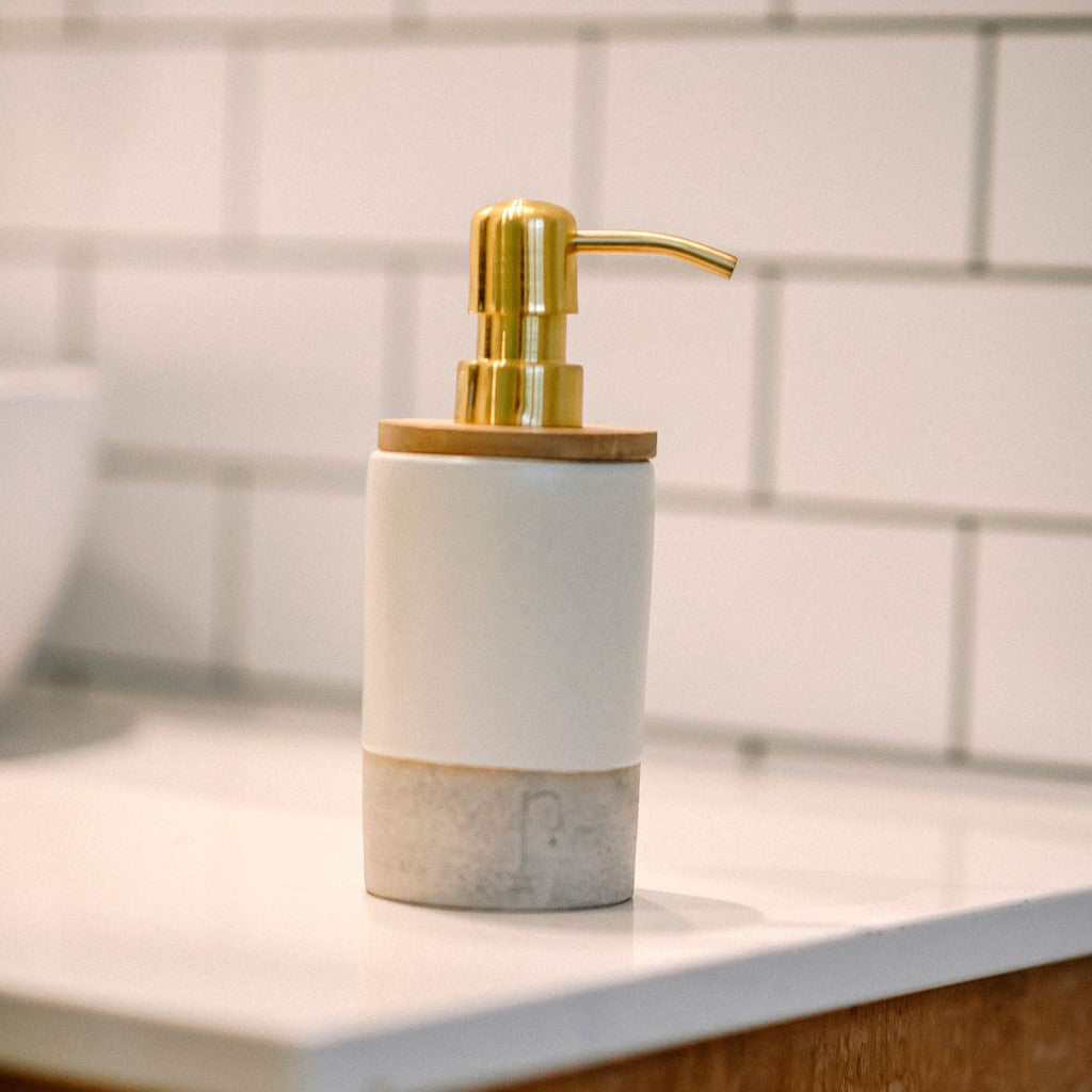 Pompe à savon en céramique de couleur or sur comptoir en marbre.