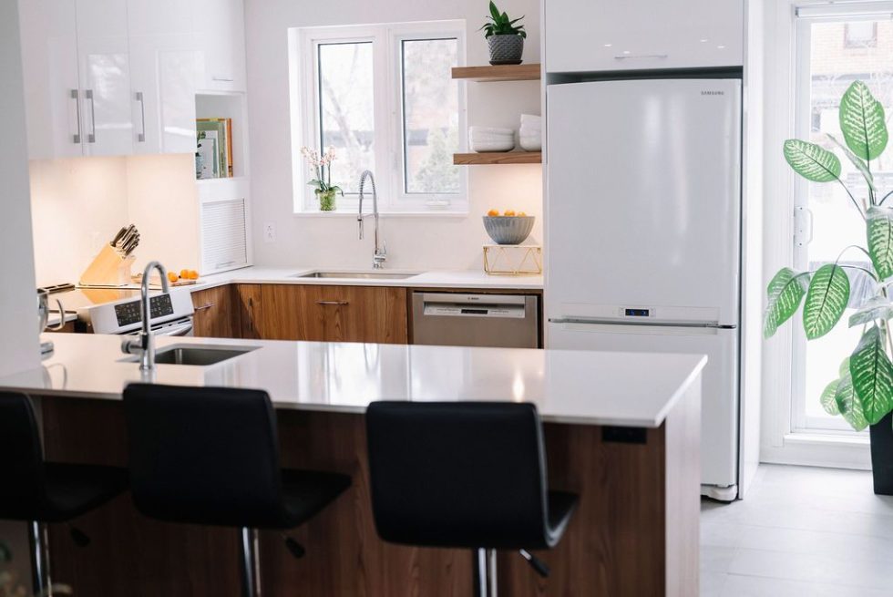 une cuisine avec un plan de travail blanc et des chaises noires.