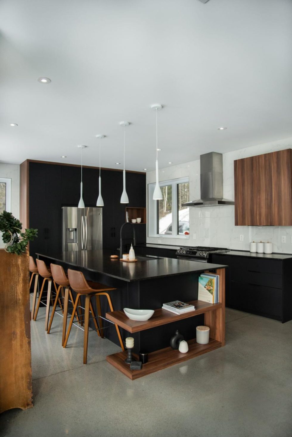 Cuisine moderne avec comptoirs noirs, armoires en bois et appareils électroménagers en acier inoxydable. Comprend un grand îlot avec tabourets de bar et luminaires suspendus au-dessus.