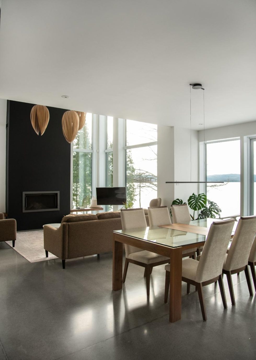 Un salon et salle à manger moderne avec de grandes fenêtres, des meubles aux tons neutres, une cheminée minimaliste et une vue sur un lac à l'extérieur.