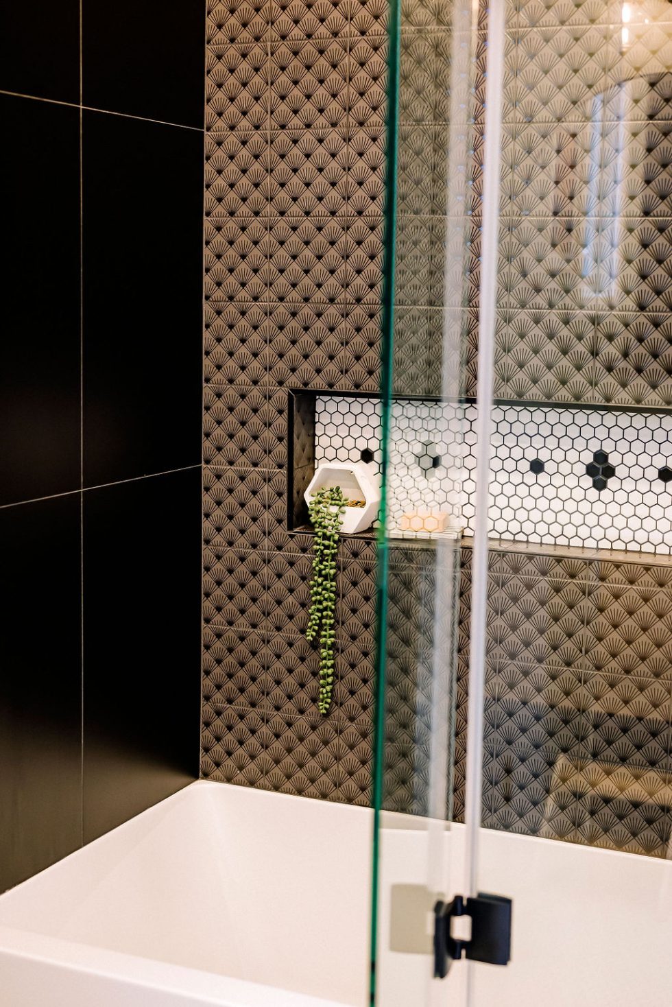 Une salle de bain moderne dispose d'une niche murale en carrelage géométrique avec une plante et une baignoire blanche.